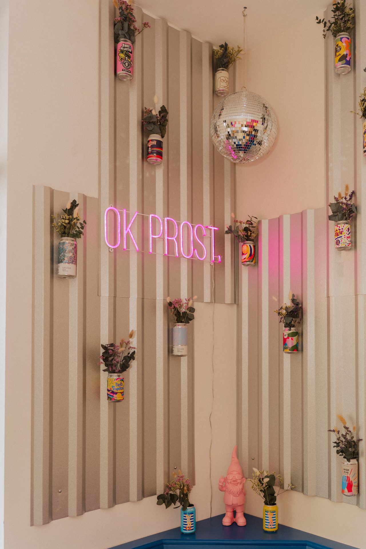 OK PROST.-Neonschild, Discokugel und Wand voller bunter Dosen mit Trockenblumen